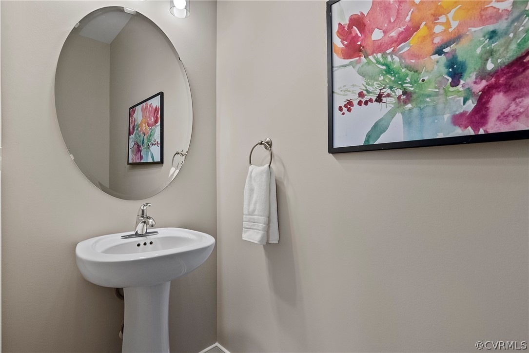 Powder room with pedestal sink, round mirror, and colorful artwork